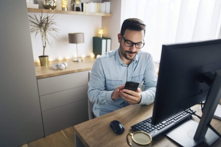 Smiling handsome freelancer working remotely from home. He is using phone.